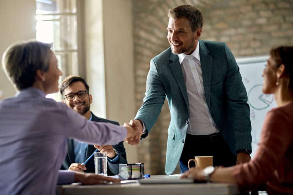 business coworkers shaking hands meeting office focus is businessman scaled